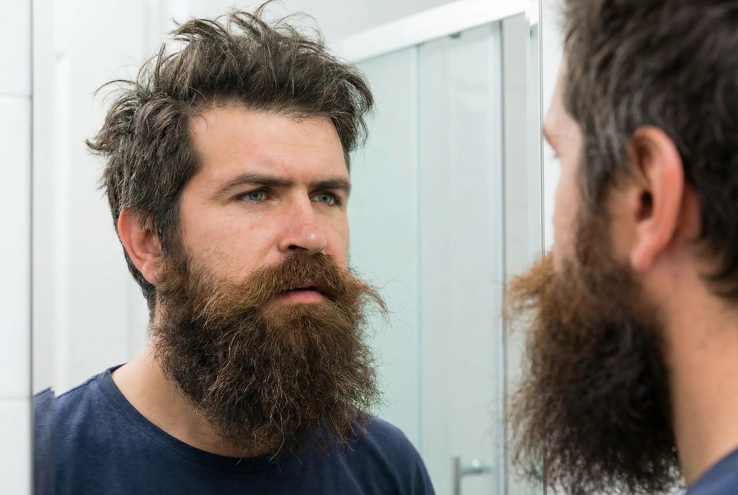 Man met volle baard kijkt in de spiegel en denkt hoe moet ik mijn baard stylen