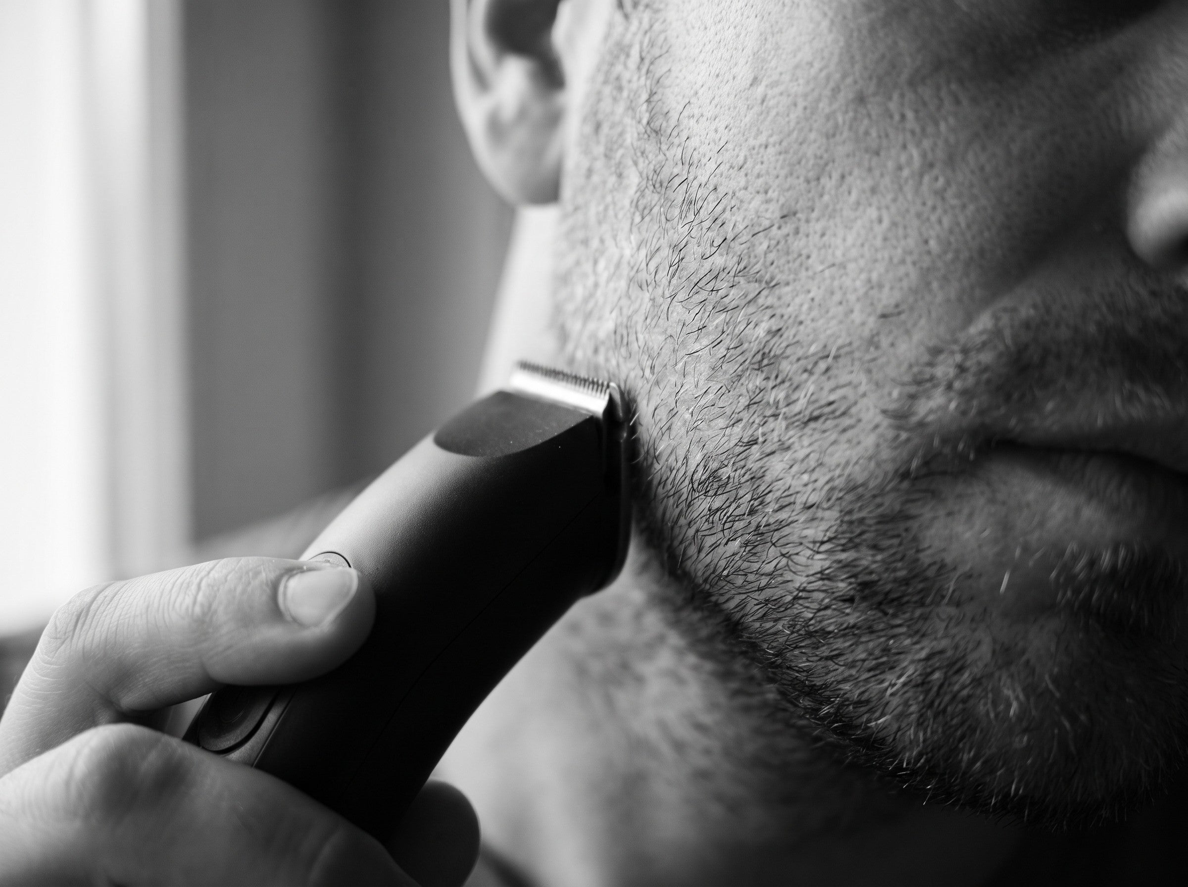 Close-up of a man maintaining his stubble beard with a precision trimmer along the jawline