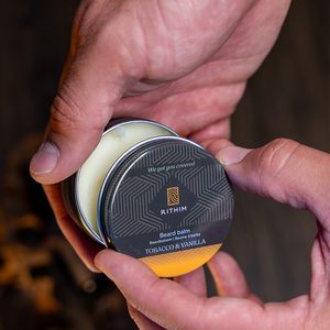 A close-up of a person's hands holding an open round tin of RITHIM Tobacco Vanilla beard balm
